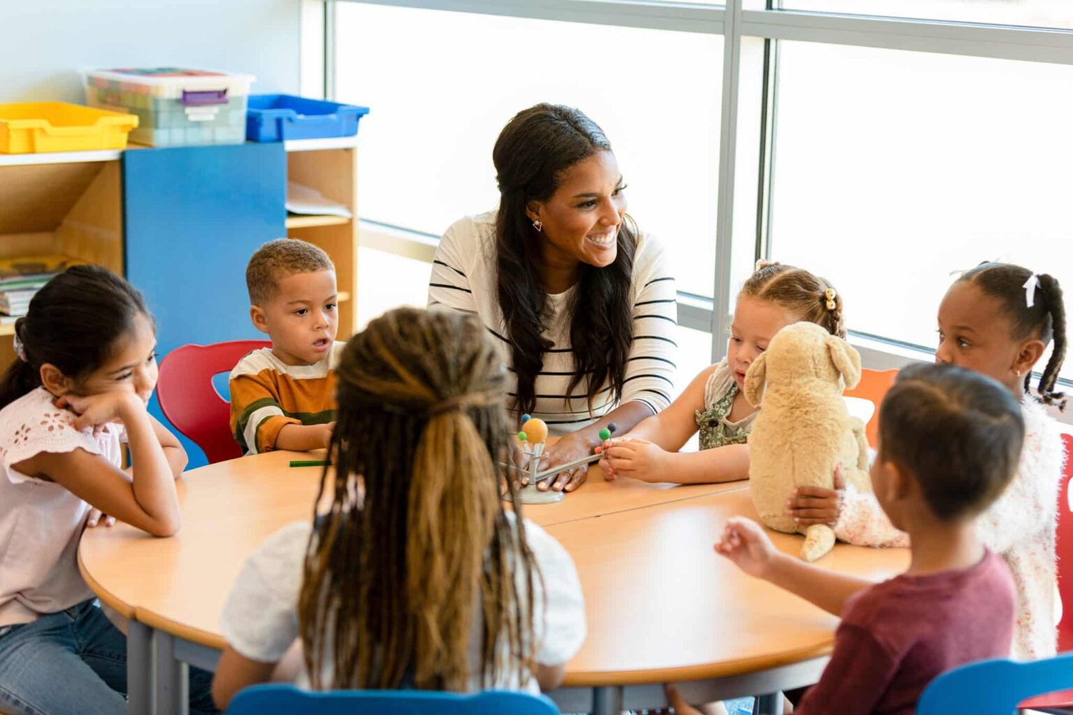 speech-delay-treatment Teacher of small children at a table showing 6 seated children a small model of the solar system.