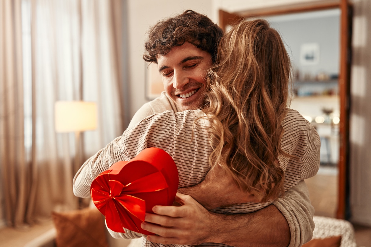 Man holding a heart-shaped valentine's box hugging his partner